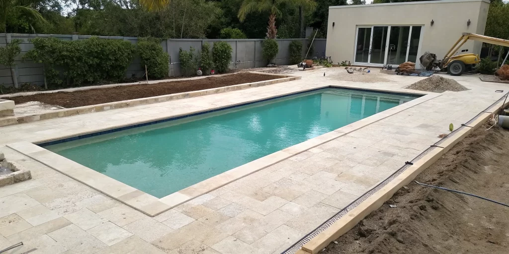 Travertine pool deck installation with pavers being laid around a swimming pool.